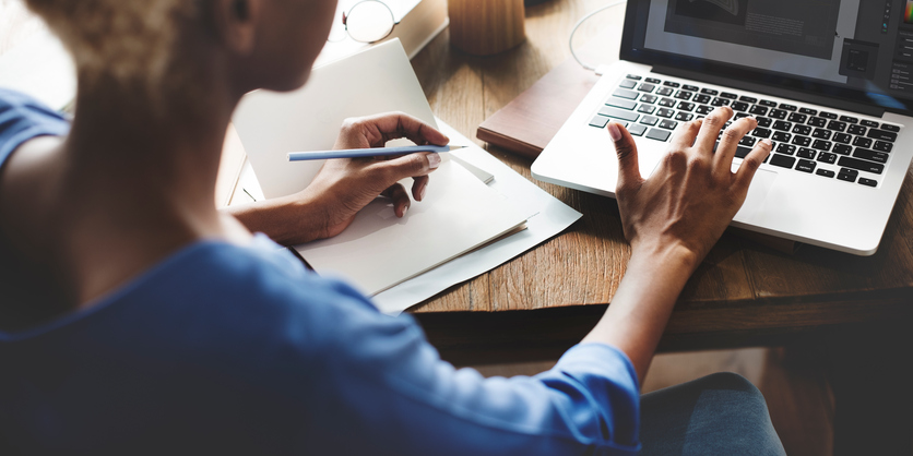 Image of woman on laptop from behind; she is taking notes as well, meant to illustrate user documentation.