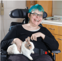 A young woman rocking a blue pixie haircut laughs at a joke while sitting with her pet bunny at home.