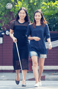 Lisa, a customer who is blind, being led to a sighted person while also using a cane 