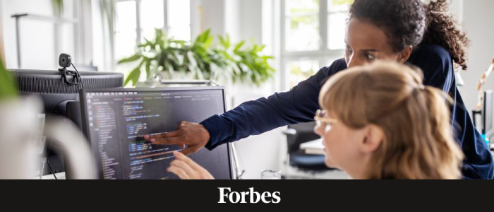 Two women collaborating at a computer, with a Forbes logo