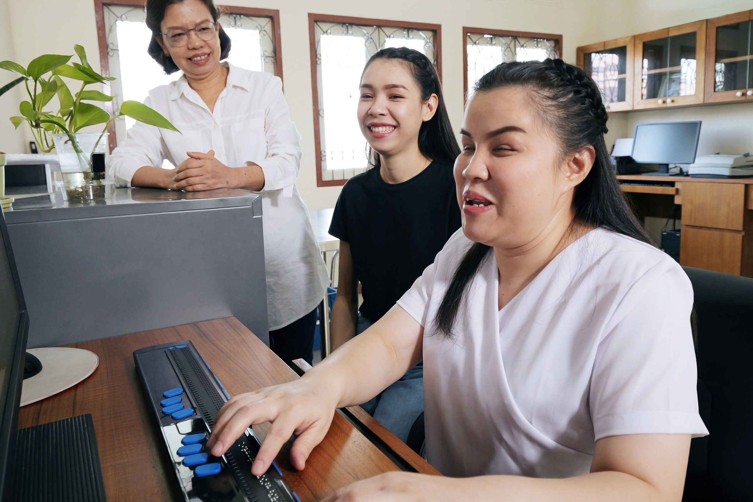 A braille keyboard user performing and audit, surrounded by two colleagues.