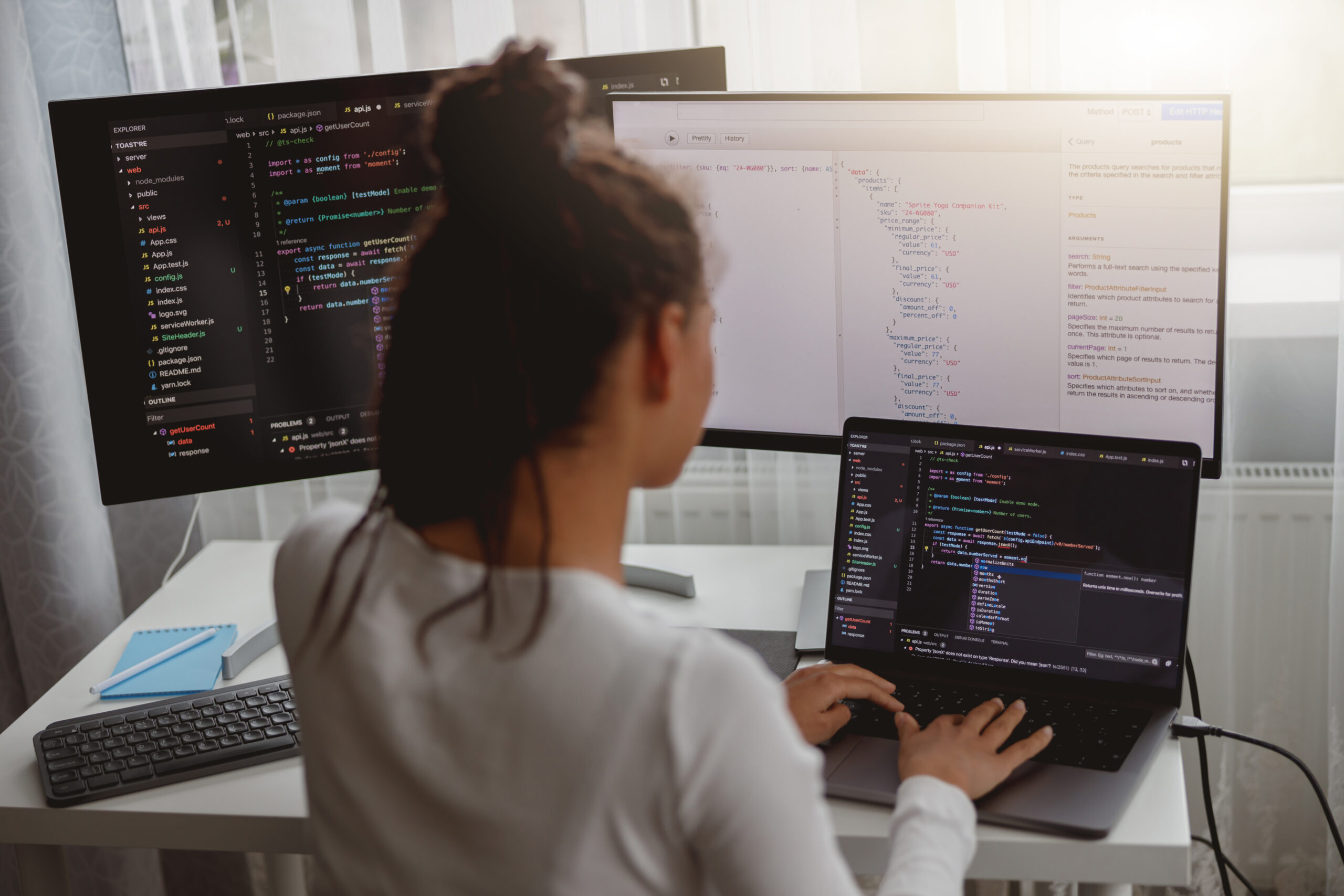 Women working on a laptop at a desk with 2 monitors on it.