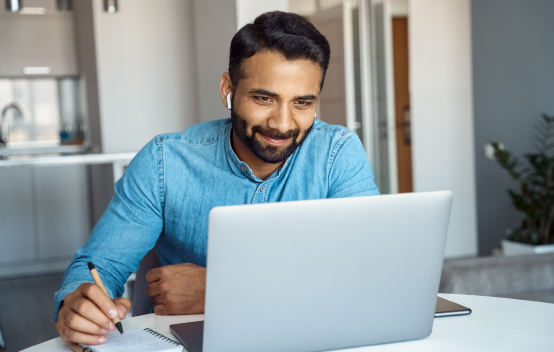 man looking at laptop screen and writing notes on a notepad
