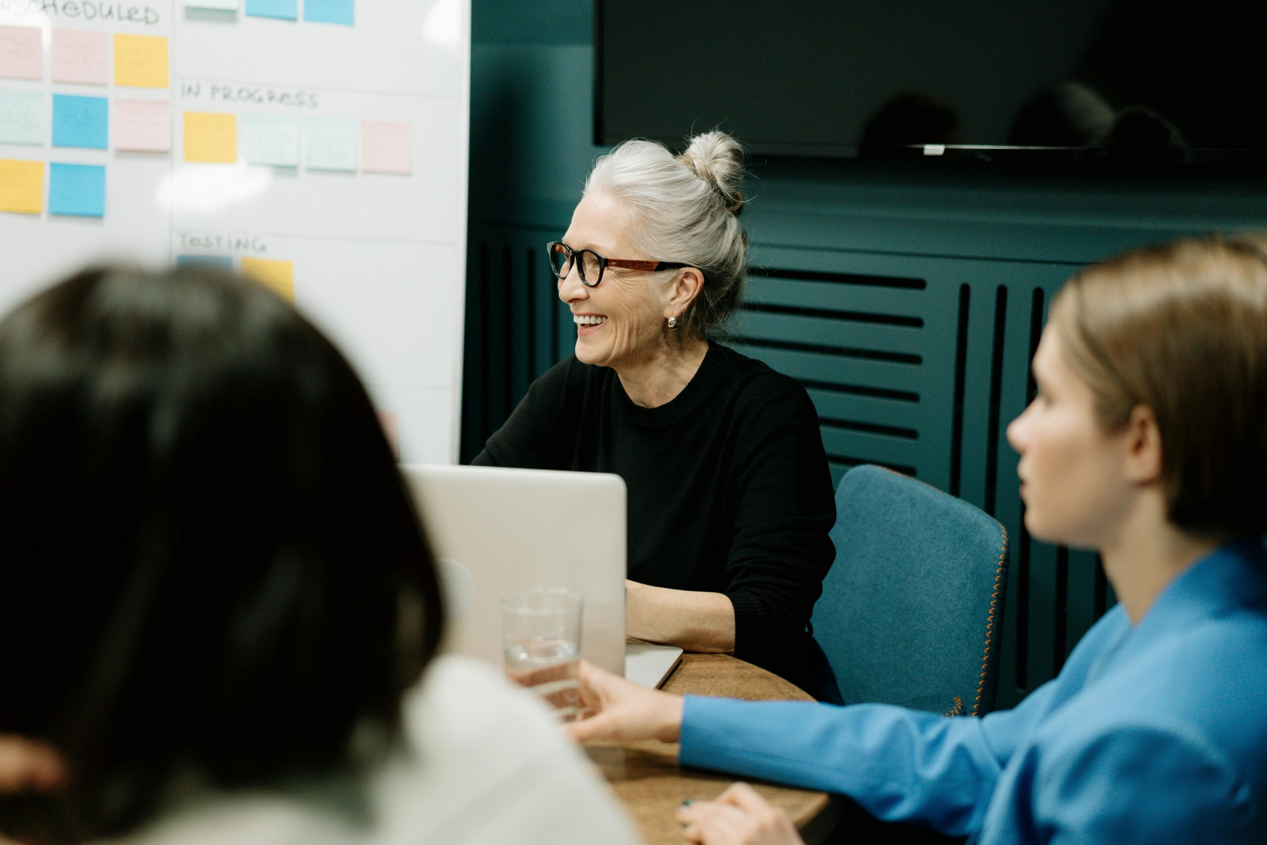 woman smiling to a group of people with a board of post-it notes behind her