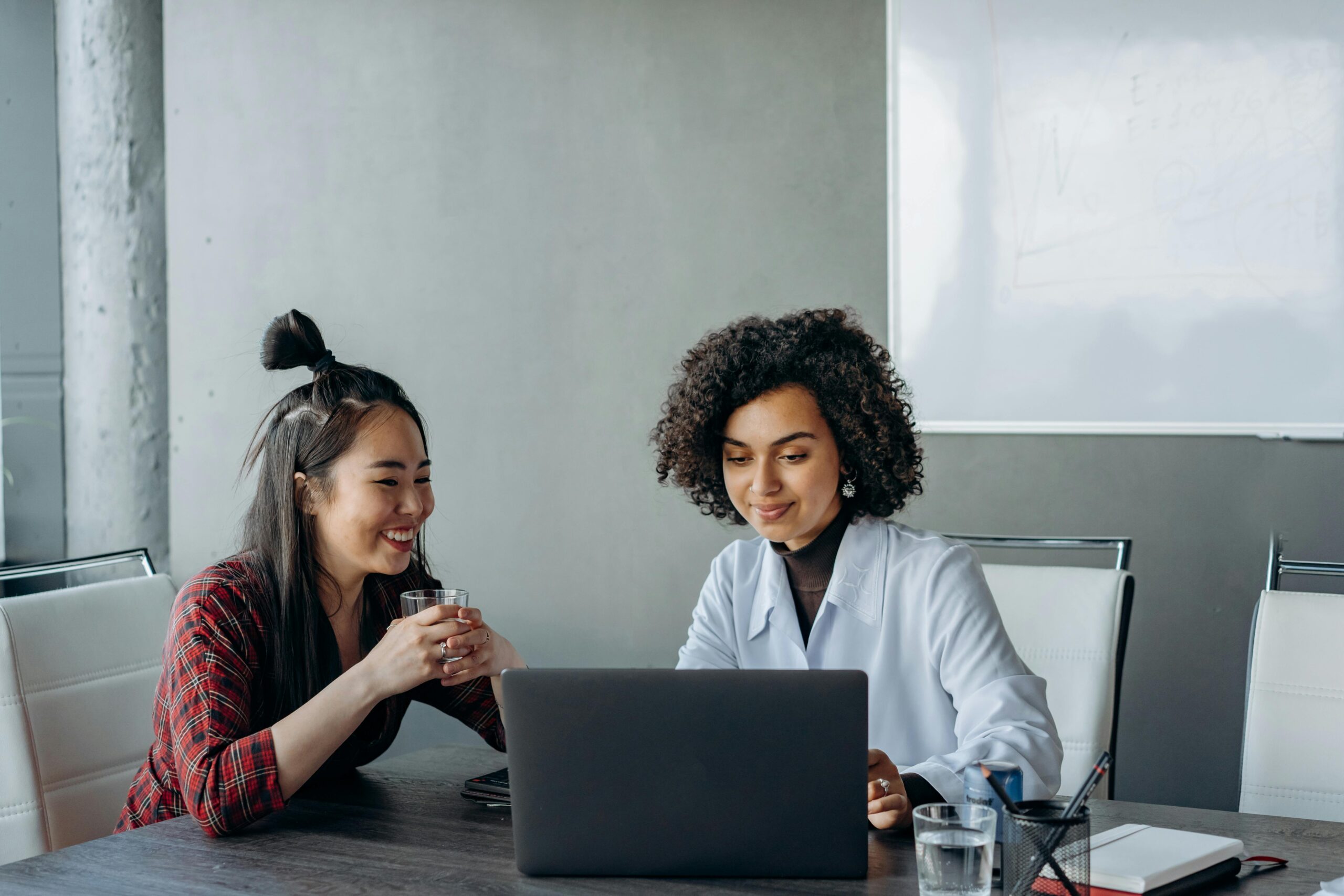 two women sitting at a table looking at a laptop computer
