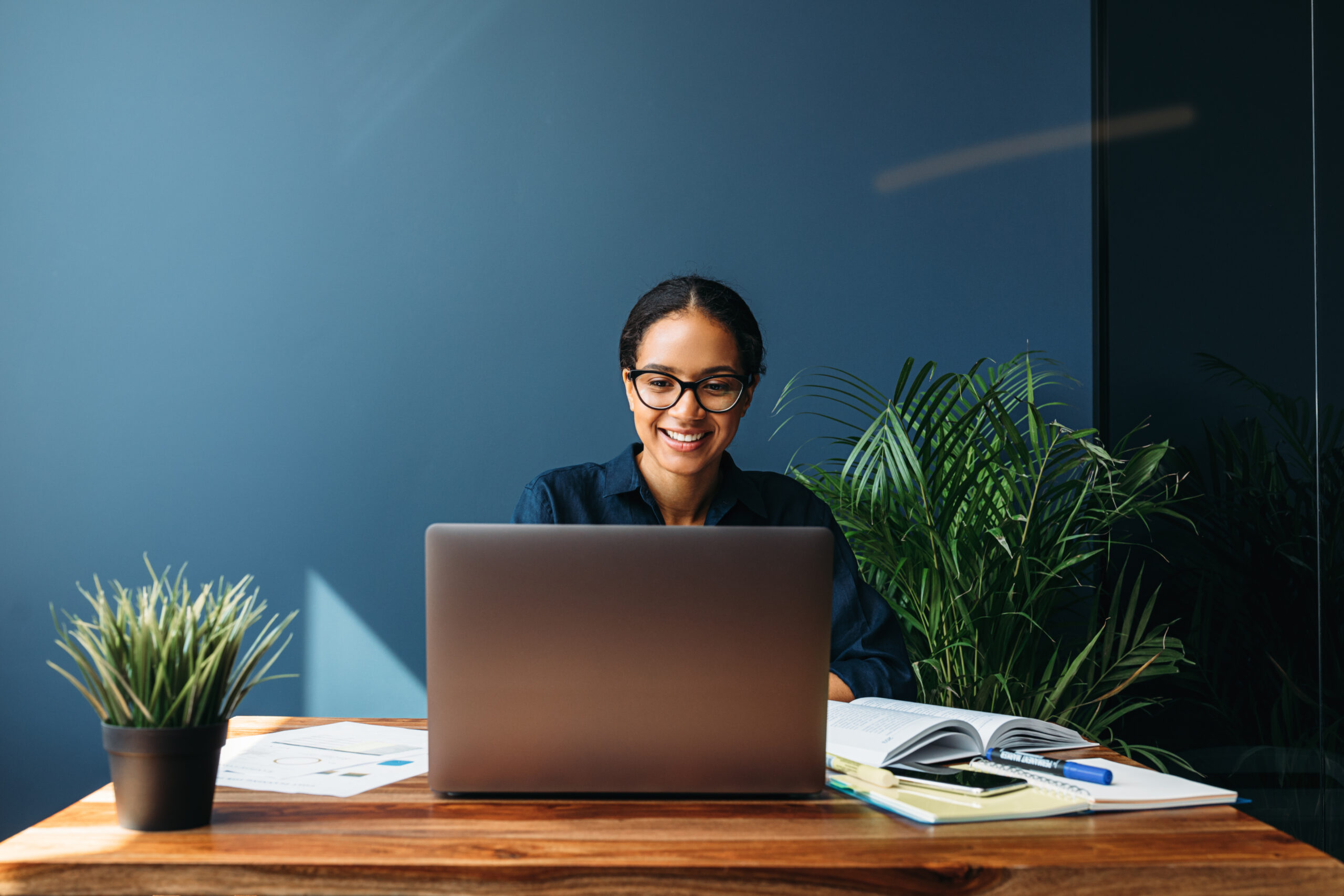 Smiling woman with glasses working on a laptop at her desk