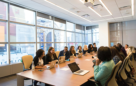 A large conference room with a dozen people and their laptops collaborating together
