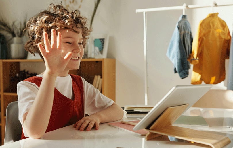 A young student greeting others virtually through a tablet